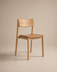 The Poise Dining Chair | Leather by Wooden Stories features a minimalist solid oak frame with a curved backrest and a flat leather seat, presented against a neutral beige background.