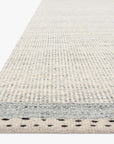 A close-up of the Loloi Sloane Rug - Sky showcases its light, hand-woven texture with subtle gray stripes and a dotted border, set against a white background. This contemporary bohemian rug seamlessly combines pattern and texture for a stylish finish.