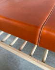 Close-up of the SOBU Cesco Bench - White Ash, showcasing a smooth tan top grain leather cushion with visible stitching atop a light slatted solid American ash base, set against a gray concrete floor.