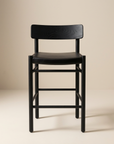 The Cesco Counter Stool by SOBU features a modern design in black ash, with a rectangular backrest, a flat top grain leather seat, and straight legs crafted from solid American ash. It is photographed against a plain beige background.
