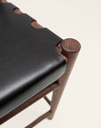 Close-up of the SOBU Cesco Counter Stool - Walnut, featuring a smooth top grain leather seat with rounded cutouts, set on a solid American Eastern black walnut frame with rounded legs and minimalist style.