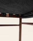 Close-up of the underside of the SOBU Cesco Counter Stool - Walnut, highlighting its solid American Eastern black walnut frame, joints, support beams, dark fabric upholstery, and a small square metal logo plate.