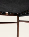 Close-up of the underside of the SOBU Cesco Counter Stool - Walnut, highlighting its solid American Eastern black walnut frame, joints, support beams, dark fabric upholstery, and a small square metal logo plate.