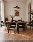 A rectangular Leviathan Live Edge Dining Table - Wood Legs surrounded by six black armchairs in a sunlit room.