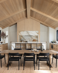 Certainly! Here is a rewritten version of the sentence, incorporating your product data: A modern kitchen and dining area featuring wood ceilings, a striking SOBU Mars Live Edge Dining Table in white ash with brass T legs as the centerpiece, surrounded by six black chairs, marble accents, large windows, and neutral-toned cabinetry.