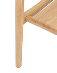 Close-up of a light oak leg from the Wooden Stories Poise Dining Chair, seamlessly attached to a matching shelf with visible wood grain and a smooth finish.