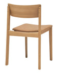 The Wooden Stories Poise Dining Chair in Light Oak with Leather features a curved wooden backrest and a light brown padded seat, shown from the rear against a white background.