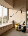 A cozy modern room with large windows, a wood-paneled wall, a cushioned bench, the SOBU Viking Lounge Chair in walnut with a mustard yellow throw, a small side table, and a black wall lamp. Natural light fills the space.