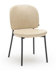 The Solace Dining Chair | Leather by Wooden Stories features a modern upholstered beige seat, rounded backrest, and four slim black metal legs, displayed against a white background.