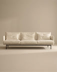 The Cherry Sofa | Fabric by SOBU is a modern cream 3-seater with Danish lines, three seat and back cushions, slim black metal legs, and a minimalist design—perfect for any contemporary living space. Plain beige background enhances its sleek look.