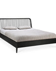 The Spindle Bed - Black Oak by Ethnicraft, made from solid European oak with a spindle headboard, is shown with a light gray mattress and two matching pillows on a white background.