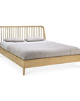 The Ethnicraft Spindle Bed - Oak features a slatted headboard in light European oak, shown with a gray blanket and two matching pillows.