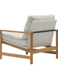 The Troubadour Lounge Chair | Fabric by Wooden Stories features a solid oak frame, sleek black metal support bar, and light gray upholstered cushions, shown from a rear side angle on a white background.