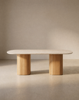 The Tathra Ellipse Dining Table by Wooden Stories features a minimalist stone oval top and two solid oak cylindrical legs, reflecting European craftsmanship against a neutral beige background.