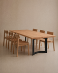 The SOBU Tommaso Dining Table, with curved metal legs, is paired with six matching wooden chairs and set in a minimalist, neutral-toned room.