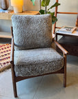 The Viking Lounge Chair - Walnut by SOBU, featuring plush textured gray cushions, sits beside a wooden table, plant, and lamp on a tiled floor—showcasing mid-century modern style in this cozy, well-lit room.