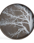 The Ethnicraft White Tree Wooden Tray - Round / Large features a dark wooden surface with a silver, intricate tree branch silhouette silk-screen printed over it, offering a nature-inspired design against a plain white background.