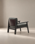 A contemporary Wren Lounge Chair by Wooden Stories, featuring a solid walnut frame, gray fabric upholstered seat and backrest, and a brown leather accent on the reverse side, displayed against a plain beige background.