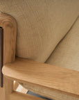 Close-up of the Wren Lounge Chair | Fabric by Wooden Stories, expertly crafted from solid walnut with light beige upholstery. The smooth wood grain and textured fabric are showcased, while the chair rests on a neutral-colored carpet, capturing the timeless elegance inspired by Danish furniture design.