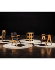 Four Dolores Chairs by Noir Trading Inc., each with distinct mid-century style, are displayed on separate circular white spots atop a concrete floor against a dark backdrop.