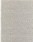 A close-up of the Andes Rug - Parchment by Armadillo&Co shows its textured, light beige wool surface with a subtle repeating pattern, highlighting the edge of this handmade piece against a plain background.