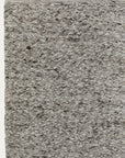 A close-up of the Andes Rug - Pumice from Armadillo&Co highlights its textured, braided pattern in gray and white tones. The woven design stands out against an off-white background.