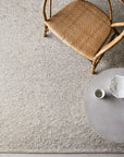 A top-down view of a woven chair next to a round, light table with a small bowl and cup, all placed on the textured Andorra Rug - Terrazzo by Armadillo&Co.