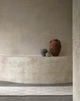 Three clay vases in brown, gray, and beige rest on a curved shelf against a textured beige wall in a softly lit minimalist room, grounded by the Armadillo&Co Atlas Rug in Limestone.