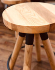 A close-up of the SOBU Blix Counter Stool, featuring a round, light wood seat and angled legs on a wooden floor. Another Blix Counter Stool is blurred in the background.