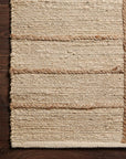 A close-up of Lolois Bodhi Rug - Ivory / Natural Grid shows its 100% jute, natural woven texture and grid pattern with horizontal braids, beautifully displayed on a dark wooden floor.