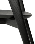 Close-up of Ethnicraft’s Bok Dining Chair - Black Oak, highlighting the angled leg, seat, and side support in solid oak with a textured wood grain finish.