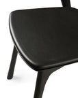 Close-up of the Ethnicraft Bok Dining Chair—Black Oak with Leather—highlighting its smooth, leather seat and solid oak legs, echoing fine craftsmanship and modern design.