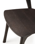 Close-up of the Ethnicraft Bok Dining Chair - Brown Oak, crafted from solid oak with a dark finish. The seat and three angled legs contrast a white background, highlighting the wood grain and smooth, modern design.
