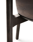 Close-up of the Bok Dining Chair - Brown Oak by Ethnicraft, showing the joint where seat meets leg and support, with detailed wood grain and craftsmanship.