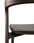 Close-up of the Ethnicraft Bok Dining Chair—Brown Oak with Leather—showing its curved solid oak backrest and padded dark brown semi-aniline leather seat, set against a white background.