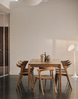Minimalist dining room with an Ethnicraft solid oak table, six Ethnicraft Bok Dining Chairs - Oak, two ceramic vases, a white modern floor lamp, and neutral walls illuminated by natural light.