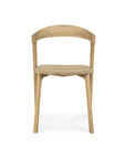 The Ethnicraft Bok Dining Chair - Oak features a minimalist design with a curved backrest, straight front legs, and angled back legs. Crafted from solid oak with a smooth natural finish, its shown on a white background.