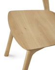 Close-up view of the Ethnicraft Bok Dining Chair - Oak, showcasing its light solid oak seat, angled legs, and minimalist design that emphasizes the natural wood grain.