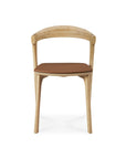 The Ethnicraft Bok Dining Chair - Oak with Leather is shown from the front, highlighting its solid oak frame, curved backrest, and brown Nappa leather cushioned seat against a white background.