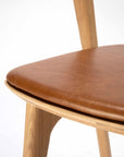 Close-up of the Ethnicraft Bok Dining Chair - Oak with Leather, showing its smooth Nappa leather seat cushion and solid oak legs against a plain white background.