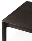 A close-up of the Ethnicraft Bok Dining Table in Brown Oak showcases its clean, modern lines and smooth finish, with the dark European oak corner set against a white background.