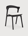 The Ethnicraft Bok Outdoor Dining Chair in black teak features a curved backrest and white cushioned seat, made from FSC certified wood, shown against a plain white background.