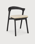 The Ethnicraft Bok Outdoor Dining Chair in black teak features a matte FSC-certified frame, curved backrest, and light beige seat cushion, shown against a plain white background.