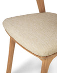 Close-up of the Ethnicraft Bok Outdoor Dining Chair in natural FSC-certified teak, featuring light beige textured upholstery. Only part of the seat, legs, and backrest are shown against a white background.