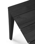 Close-up of the Ethnicraft Bok Outdoor Dining Table in black teak, featuring angled legs and three slats on its Grade A teak top, shown against a white background.