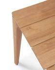 Close-up of the Ethnicraft Bok Outdoor Dining Table in natural teak, featuring angled legs and a smooth, slatted surface, shown against a white background.