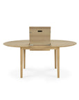 The Bok Round Extendable Dining Table - Oak by Ethnicraft is a light wood, four-legged round table with a central leaf panel that can be partially raised to extend its length.