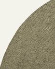 Close-up of the Armadillo&Co Braid Rug - Oregano, a round, handmade wool-blend piece in a neutral greenish-brown hue with visible braided patterns, partially displayed on a plain off-white background.