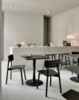 Minimalist café interior featuring dark wooden tables and Ethnicraft’s Casale Dining Chair in black, a light-hued countertop, and neutral walls. The counter displays pastries, fruits, drinks, glassware, and a contemporary table lamp for a calm vibe.
