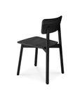 The Casale Dining Chair - Black by Ethnicraft is a minimalist European oak chair with clean lines, a slightly curved backrest and seat, and four sturdy legs—shown angled on a white background, ideal for pairing with Ethnicraft dining tables.